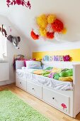 Bed with white wooden frame and drawers in child's attic bedroom