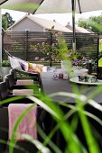 Cups, tealight holders and bouquet of garden flowers on table below parasol on terrace; hammock in background