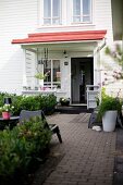 Secluded seating area on paved terrace outside white clapboard house with porch