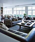 Verschiedene Sofa aus Leder und grauem Samtstoff um Couchtisch, in offenem Wohnraum mit weissen Terrassentüren