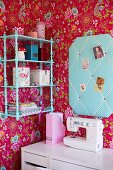 Tapezierte Zimmerecke eines Mädchenzimmers mit Blumenmuster auf pinkfarbenem Hintergrund, Pinnwand mit türkisem Stoffbezug, abgestimmt mit Farbe vom Wandbord