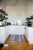 Schwarz-weiss gemusterter Teppichläufer auf Fischgrätparkett in offener weisser Designerküche
