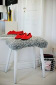 Red slippers on stool with grey, fur-like cover in front of mirror on wall