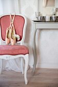 Ballet shoes on Rococo-style chair with pink velvet cover next to console table with curved legs