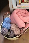 Balls of wool in various colours and pink blanket in basket on floor