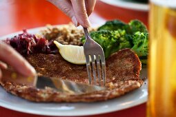 Escalope á la viennoise being sliced. Served with broccoli and red cabbage