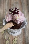 A chocolate cupcake topped with blueberry cream with a bite taken out