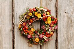 Herbstlicher Kranz aus Strohblumen und Früchten an Holzbretterwand aufgehängt