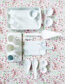 Various glasses, cup, bowls and a serving platter on a floral-patterned tablecloth