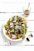 Vegetable salad (kohlrabi, yellow pepper, carrots, rocket) with parsley, basil and pansies