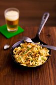 Cheese Spätzle (soft egg noodles from Swabia) in a pan with a glass of beer in the background