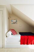 Bolster, scatter cushions and blanket on bed in niche below sloping attic ceiling