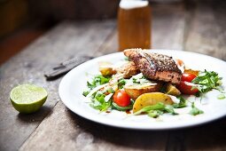 Grilled Cajun salmon steak on a bed of potato wedges and rocket and tomato salad with Parmesan