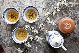 Drei asiatische Teeschälchen mit Grüntee , Teekanne und Kirschblütenzweig