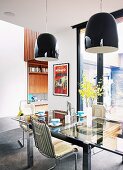 Black, reflective pendant lamps above original 60s, chrome cantilever chairs and glass table in dining area