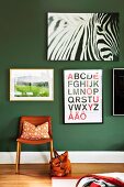 Various posters on dark green wall above leather chair and handbag on floor