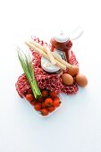 A net shopping bag with tomatoes, chives, bread sticks, eggs and sauces