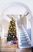 View through arched, open doorway of decorated Christmas tree next to white, wooden staircase in foyer