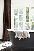 Free-standing, anthracite bathtub with vintage tap fittings and sunshine falling though half-open, glass French doors
