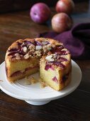 Sliced, gluten free plum cake with almonds and crumbles on a round cake plate
