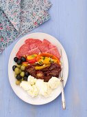An appetiser platter featuring mozzarella, olives, tomatoes, peppers and sausage