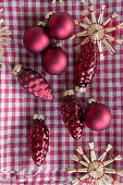 Red Christmas tree decorations and straw stars on gingham cloth
