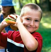 A blond boy with a burger at a picnic in a garden