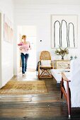 Woman in rustic living room with wooden floor; rattan armchair next to modern artwork on white wooden wall