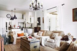 Old wooden trunk used as table and comfortable sofa set in open-plan country-house-style living area with kitchen in background