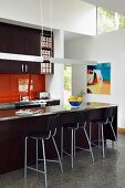 Stainless steel pendant lamps above counter with dark brown base units and bar stools