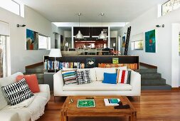 Offener Wohnraum mit Splitlevel, weiße Sofagarnitur und Holz Couchtisch auf Parkett vor Empore mit Lowboard, dahinter Ess- und Kochbereich