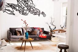 Living room with leather sofa, ethnic-style accessories, plant arrangement and artwork hanging from ceiling