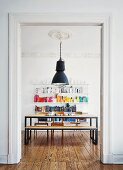 DIY, chipboard dining set with black frames below vintage industrial lamp hanging from stucco ceiling in front of colourful books on shelving