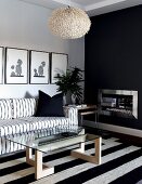 Schwarzweisser Sitzbereich im skandinavischen Stil mit Sofa und Glastisch auf Blockstreifenteppich vor anthrazitfarben getönter Kaminwand