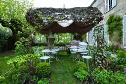 A sales exhibition of white metal furniture under a sunshade in the garden of a French country house