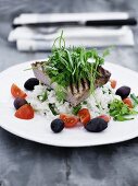 Grilled tuna steak on a bed of rice with tomatoes and olives