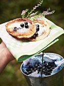 A hand holding pancakes with sugar and blueberries on a napkin