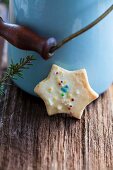 A star-shaped butter biscuit decorated with coloured sprinkles in front of a milk churn