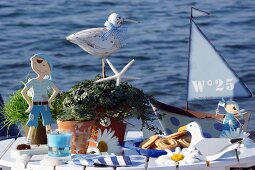 Gebäck auf Teller zwischen Deko Figuren im Seemannslook auf weißem Tisch vor Seehintergrund