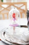 Doll under glass cover on paper doily on tray
