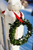 Box wreath hanging from red ribbon on snowy, vintage wooden post