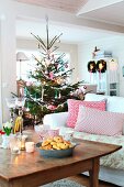 Kissen auf weißem Sofa, davor rustikaler Holz-Couchtisch, im Hintergrund geschmückter Weihnachtsbaum in ländlichem Wohnzimmer