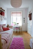 Pink flokati rug on wooden floor next to comfortable bed in child's bedroom