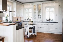 White fitted kitchen with encircling frieze, recessed lights and butchers' block trolley