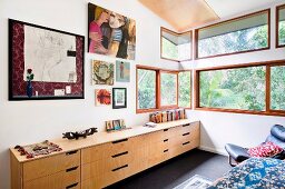 Sideboard with drawers below drawings on bedroom wall and ribbon windows with garden view