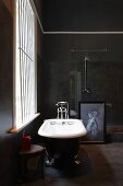 Free-standing, clawfoot bathtub next to barred window in dark bathroom