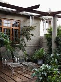 Delicate wire mesh sun loungers under pergola on terrace adjoining grey-painted house with wooden windows