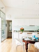 Open-plan, white kitchen with shell chairs in comfortable dining area next to open, sliding glass door