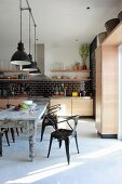 Retro metal chairs at shabby chic dining table and industrial pendant lamps with black and white lampshades in designer kitchen