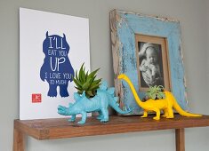 Planters shaped like miniature dinosaurs and pictures on wooden shelf
